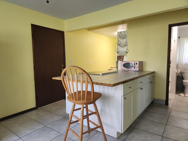 15-2687 Kaku St, Pahoa, HI 96778 - kitchen featuring white microwave, a kitchen breakfast bar, light tile patterned floors, white cabinetry, and tile counters