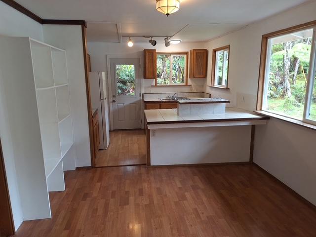 11-3791 4th St, Volcano, HI 96785 - kitchen with brown cabinets, a peninsula, light wood-type flooring, freestanding refrigerator, and a sink