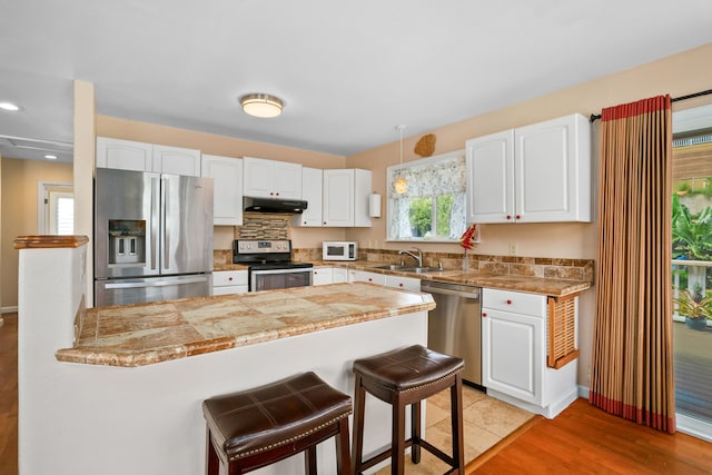 5167 Holomua Pl, Kapaa, HI 96746 - kitchen with stainless steel appliances, under cabinet range hood, a sink, a breakfast bar, and white cabinetry