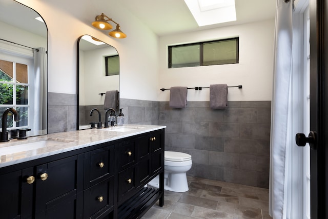 75-5811 Nani Kailua Pl, Kailua-Kona, HI 96740 - full bathroom featuring tile walls, toilet, double vanity, a wainscoted wall, and a skylight