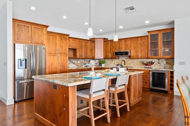 73-4566 Kukuki St, Kailua-Kona, HI 96740 - kitchen with appliances with stainless steel finishes, wine cooler, brown cabinets, a kitchen island with sink, and dark wood-type flooring