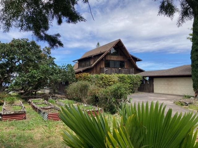 94-1790 Kaulua St, Naalehu, HI 96772 - rear view of property with a vegetable garden, concrete driveway, and an attached garage