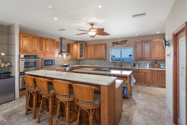 73-4571 Kukuki St Unit A, Kailua-Kona, HI 96740 - kitchen featuring a kitchen island, wall chimney exhaust hood, a sink, stainless steel appliances, and brown cabinetry