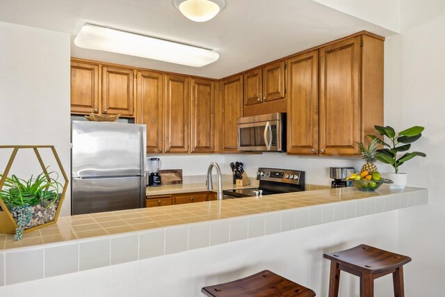 1565 Pee Rd Unit 221, Koloa, HI 96756 - kitchen with appliances with stainless steel finishes, a peninsula, brown cabinets, a kitchen breakfast bar, and tile counters