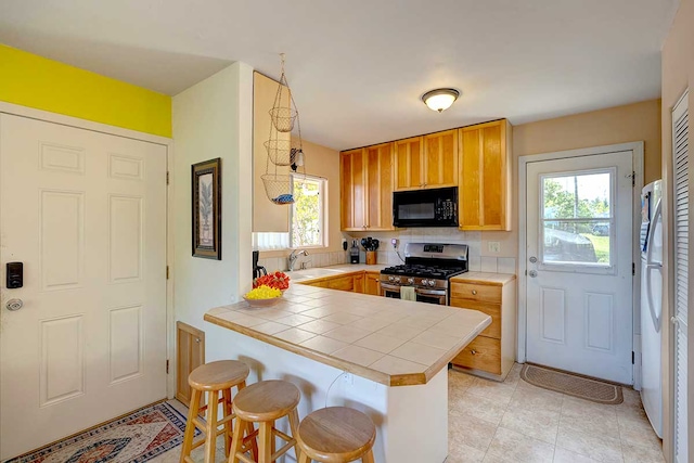 12-7036 Kaiwa St, Pahoa, HI 96778 - kitchen featuring stainless steel gas range oven, black microwave, tile countertops, a peninsula, and a kitchen breakfast bar