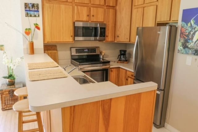 75-6016 Alii Dr Unit 108, Kailua-Kona, HI 96740 - kitchen featuring appliances with stainless steel finishes, a sink, a peninsula, light countertops, and a breakfast bar area