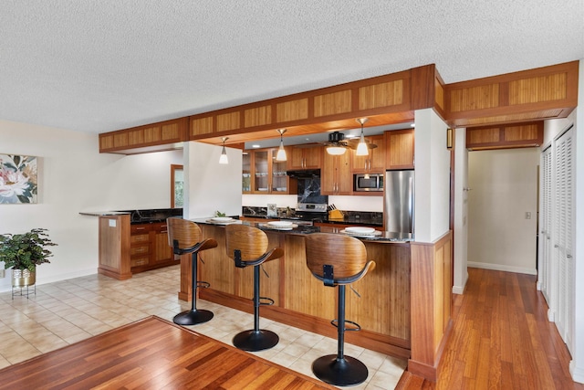 73-4332 Imo Pl, Kailua-Kona, HI 96740 - kitchen featuring stainless steel appliances, brown cabinetry, dark countertops, glass insert cabinets, and a breakfast bar area