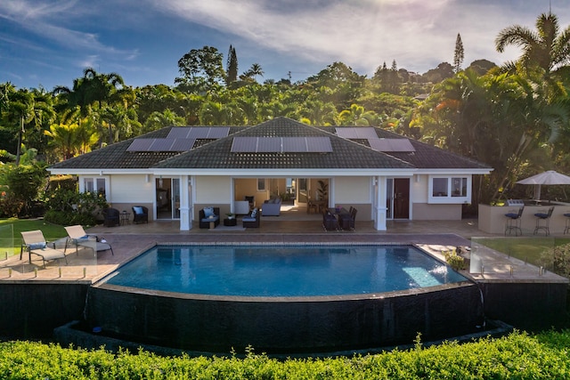 76-853 N Pakalakala Pl, Kailua-Kona, HI 96740 - back of house with a patio area, an infinity pool, roof mounted solar panels, and a tiled roof