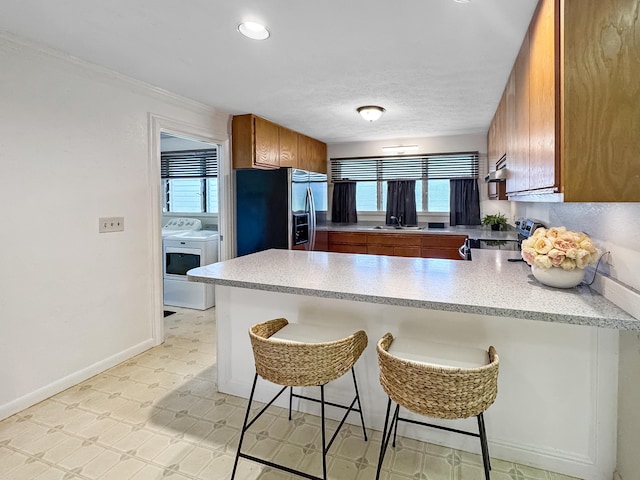 410 Olu St, Hilo, HI 96720 - kitchen featuring stainless steel appliances, washing machine and dryer, brown cabinetry, a peninsula, and plenty of natural light