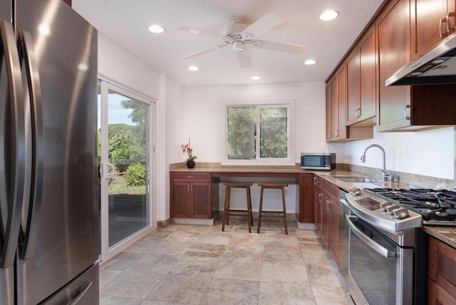 75-795 Hiona St, Kailua-Kona, HI 96740 - kitchen with stainless steel appliances, under cabinet range hood, healthy amount of natural light, brown cabinetry, and recessed lighting