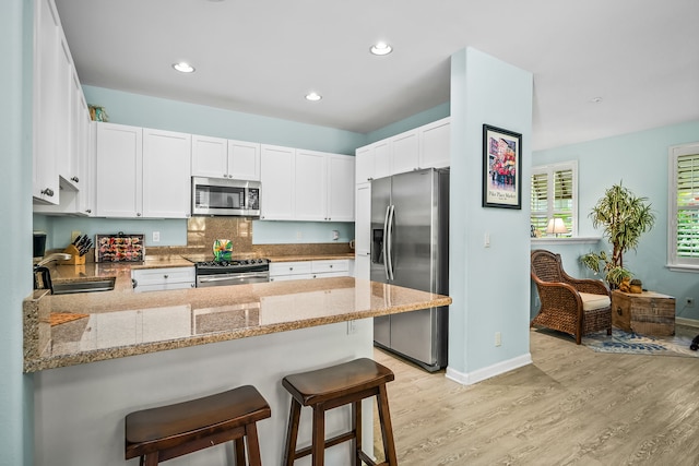 4919 Pepelani Lp Unit 2A, Princeville, HI 96722 - kitchen featuring appliances with stainless steel finishes, a peninsula, light wood-style flooring, white cabinetry, and light stone countertops