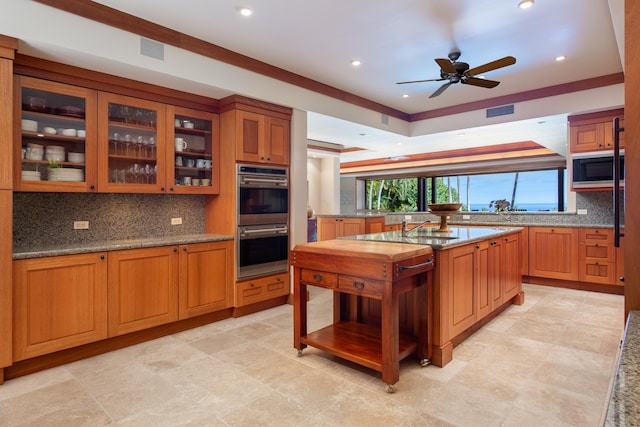 72-106 Hainoa Pl Unit 4, Kailua-Kona, HI 96740 - kitchen with stainless steel double oven, decorative backsplash, built in microwave, ceiling fan, and brown cabinets