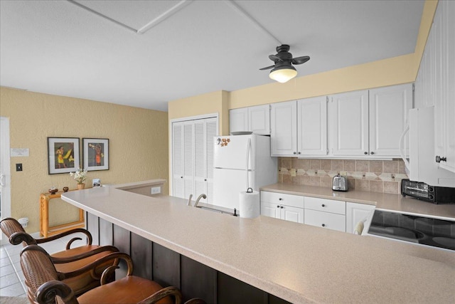 75-6016 Alii Dr Unit 323, Kailua-Kona, HI 96740 - kitchen with white appliances, a kitchen bar, a textured wall, white cabinets, and light countertops
