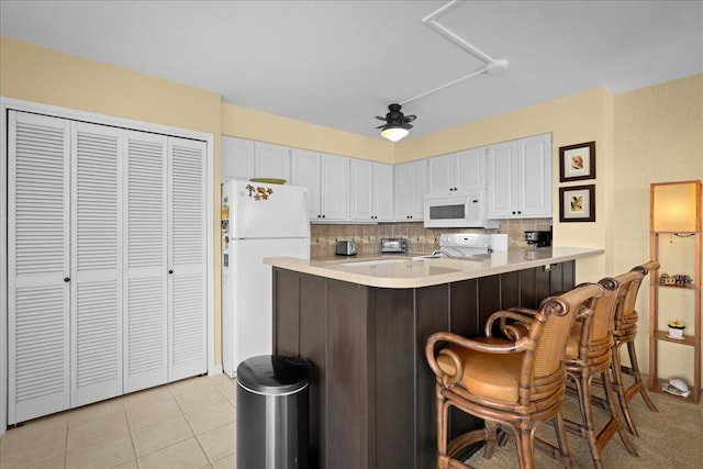 75-6016 Alii Dr Unit 323, Kailua-Kona, HI 96740 - kitchen with white appliances, light countertops, white cabinets, tasteful backsplash, and a kitchen bar