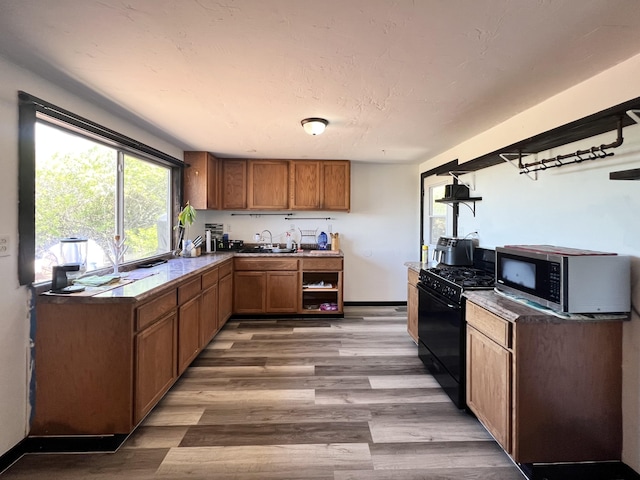 94-6347 Makai St, Naalehu, HI 96772 - kitchen featuring black gas range, stainless steel microwave, light wood-type flooring, brown cabinetry, and dark countertops