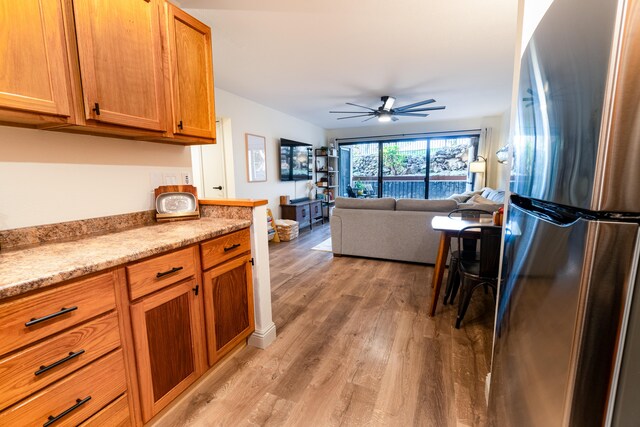 75-5863 Kuakini Hwy Unit 104, Kailua-Kona, HI 96740 - kitchen with freestanding refrigerator, light wood-style floors, ceiling fan, and brown cabinetry