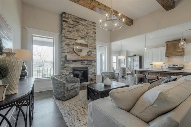 living room with an inviting chandelier, dark wood-type flooring, a fireplace, sink, and beam ceiling