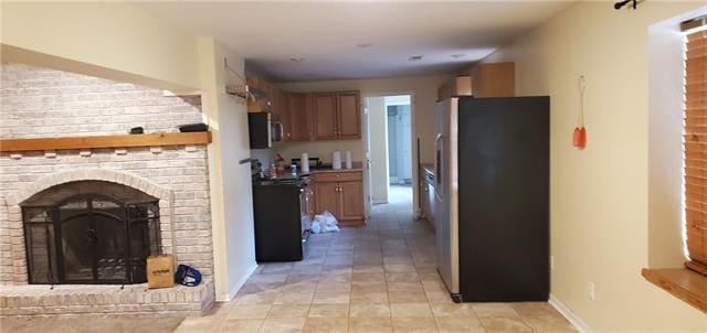 interior space with appliances with stainless steel finishes, a brick fireplace, and light tile floors