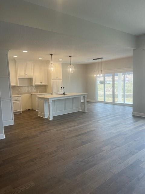 kitchen featuring sink, white cabinetry, decorative light fixtures, dark wood-type flooring, and an island with sink