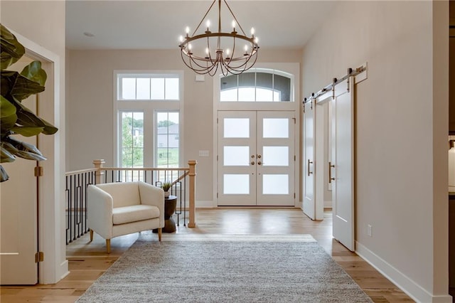 foyer entrance with a barn door, a notable chandelier, and light wood-type flooring