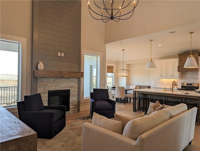 living room with a stone fireplace, sink, a high ceiling, a notable chandelier, and light wood-type flooring