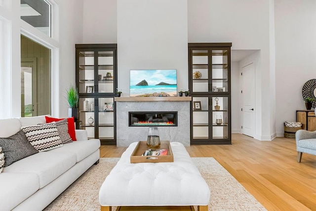 living room featuring wood-type flooring, a towering ceiling, and a high end fireplace