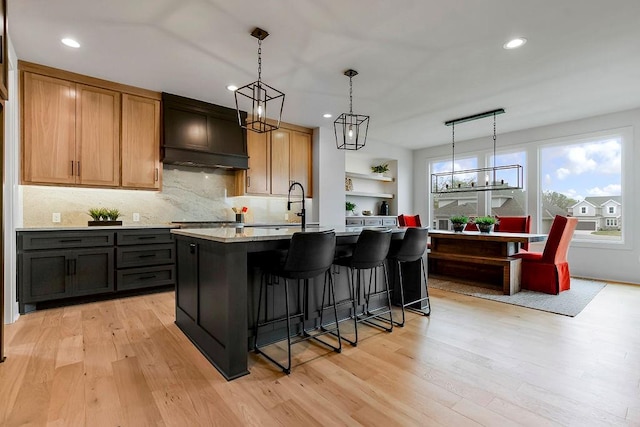 kitchen with custom range hood, light hardwood / wood-style floors, tasteful backsplash, a kitchen island with sink, and sink