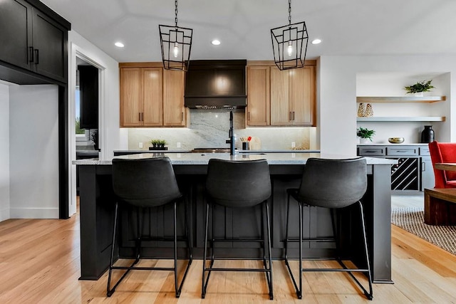 kitchen with pendant lighting, light stone countertops, light hardwood / wood-style flooring, and an island with sink