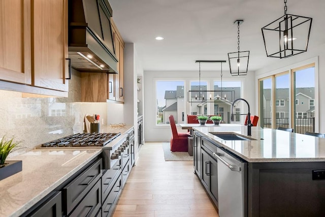 kitchen featuring light hardwood / wood-style floors, sink, an island with sink, custom exhaust hood, and decorative light fixtures