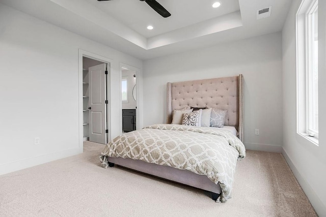 carpeted bedroom with ceiling fan, a tray ceiling, ensuite bathroom, and a walk in closet