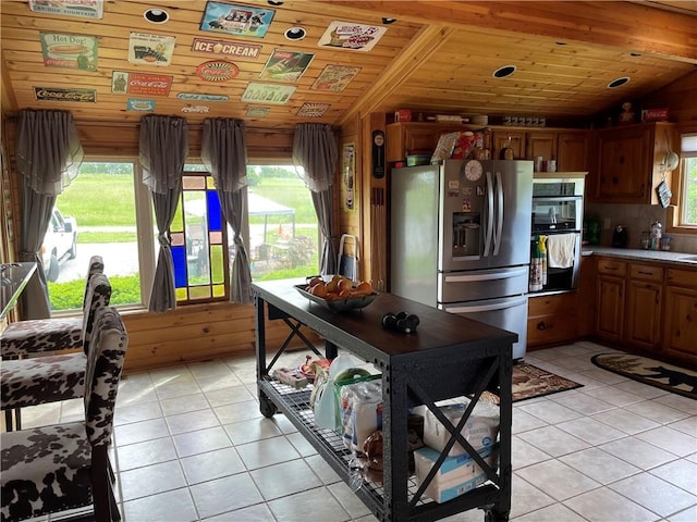 kitchen featuring vaulted ceiling, light tile patterned flooring, wooden ceiling, wood walls, and stainless steel appliances