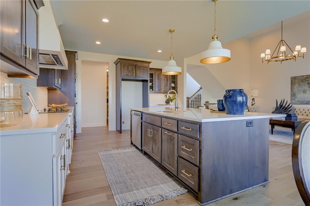 kitchen with dark brown cabinets, pendant lighting, light wood-type flooring, sink, and backsplash