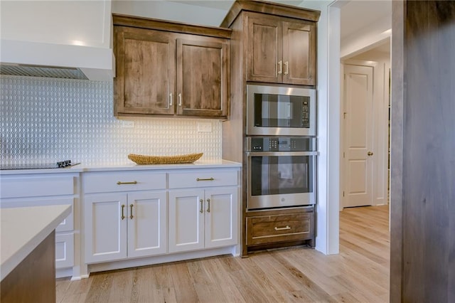 kitchen with built in microwave, light hardwood / wood-style floors, backsplash, and oven