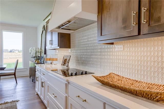 kitchen with white cabinetry, custom range hood, tasteful backsplash, black electric stovetop, and hardwood / wood-style floors