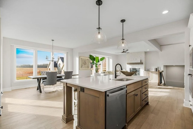 kitchen with a center island with sink, sink, light hardwood / wood-style flooring, stainless steel dishwasher, and decorative light fixtures