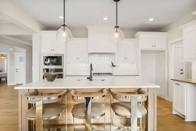 kitchen with white cabinetry, built in microwave, a center island with sink, and oven