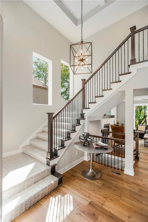 stairs featuring a towering ceiling, a notable chandelier, a wealth of natural light, and hardwood / wood-style floors