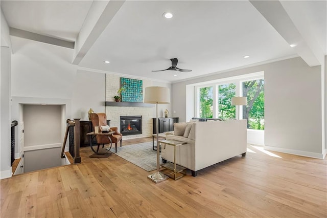 living room with ceiling fan, crown molding, light hardwood / wood-style flooring, and a stone fireplace