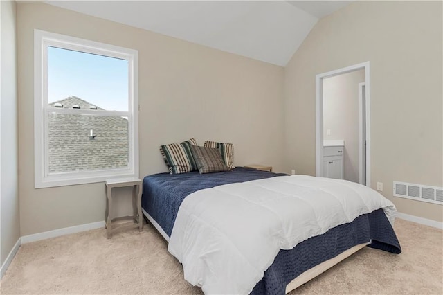 bedroom featuring light carpet, vaulted ceiling, and ensuite bath