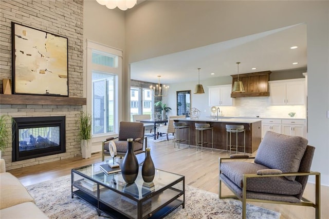 living room with a towering ceiling, sink, light hardwood / wood-style floors, a chandelier, and a multi sided fireplace