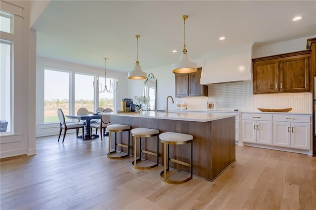 kitchen with a center island with sink, white cabinetry, decorative light fixtures, and light wood-type flooring