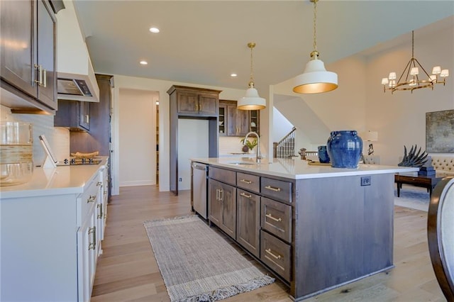 kitchen with tasteful backsplash, light wood-type flooring, dishwasher, sink, and decorative light fixtures