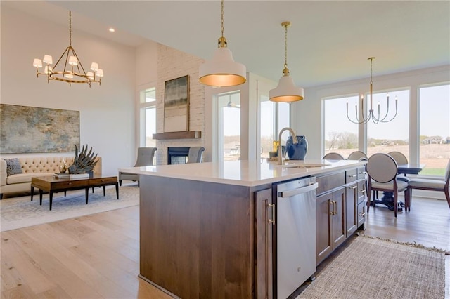 kitchen featuring dishwasher, a kitchen island with sink, sink, decorative light fixtures, and a fireplace