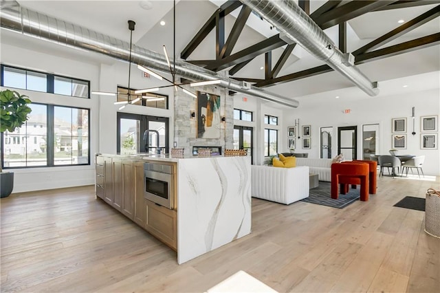 kitchen with oven, hanging light fixtures, light stone countertops, high vaulted ceiling, and light hardwood / wood-style flooring