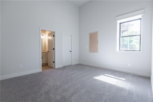 unfurnished bedroom featuring light carpet, connected bathroom, and a towering ceiling