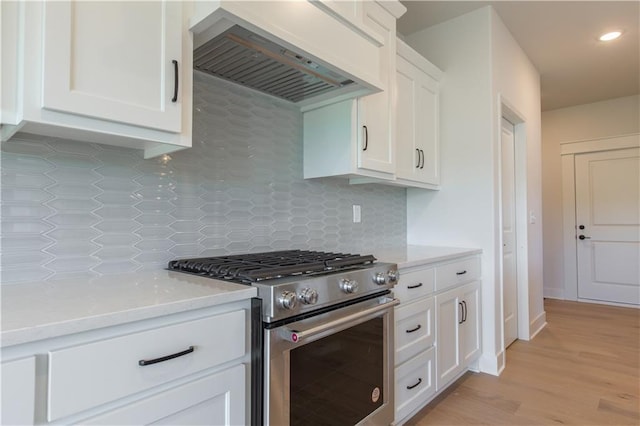 kitchen with white cabinets, light hardwood / wood-style flooring, backsplash, premium range hood, and stainless steel range