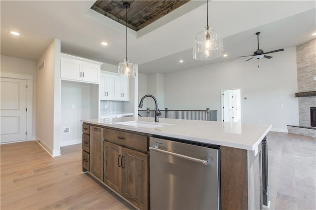 kitchen with stainless steel dishwasher, a fireplace, light hardwood / wood-style flooring, a kitchen island with sink, and white cabinets