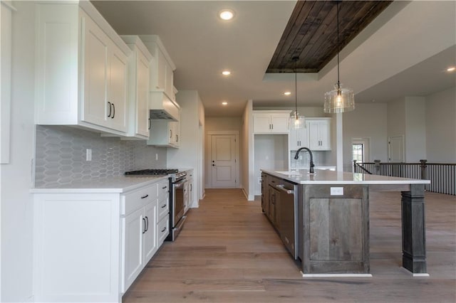 kitchen featuring a kitchen island with sink, appliances with stainless steel finishes, white cabinets, tasteful backsplash, and decorative light fixtures