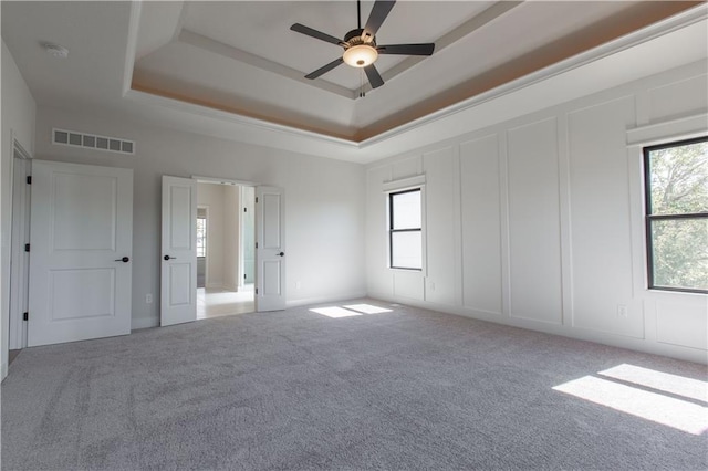 unfurnished room featuring ceiling fan, a raised ceiling, and light colored carpet