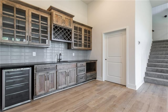 kitchen with a high ceiling, backsplash, light hardwood / wood-style floors, sink, and wine cooler